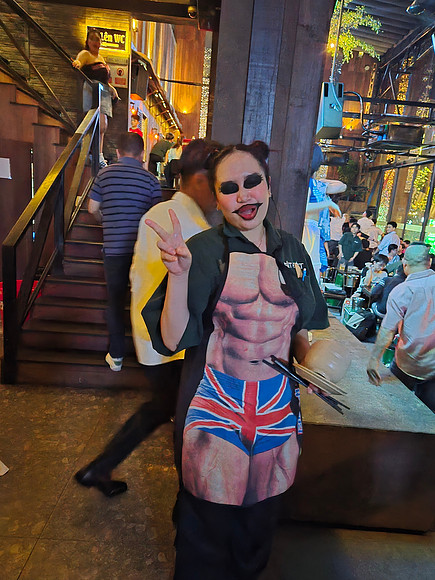 “Waitress in Union Jack pinny serving drinks at Vietnamese beer hall.”